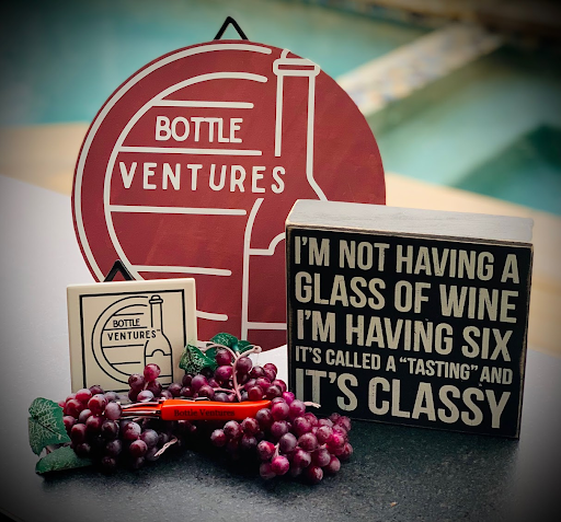 Bottle Ventures tasting props, the round brand logo sign, a playful wine sign, and grapes.